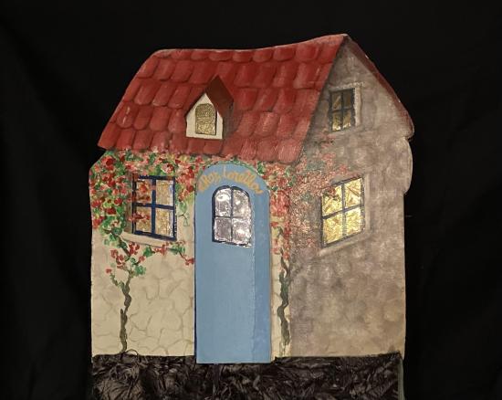 Maison à toit rouge, fenêtres dorée, porte bleue et une inscription "Chez Lorella"