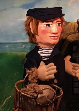 Homme brun, vêtu d'un habit de pêcheur, coiffé d'une casquette et tenant au bras un panier