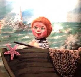 Garçon roux aux yeux bleus, vêtu d'un pull à rayures, sur la plage devant une barque