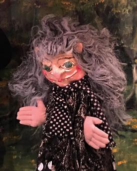 Vieille femme aux longs cheveux gris vêtue d'une robe noir et d'une écharpe à petits carreaux noirs et blancs