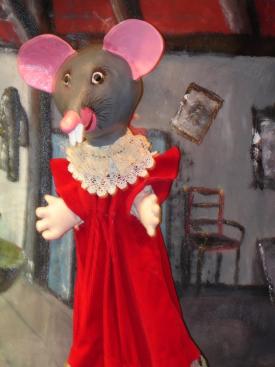 Souris grise au nez et aux oreilles roses, vêtue d'une robe rouge à col en dentelle, dans son grenier