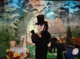 Vieil homme noiraud avec de gros favoris, vêtu d'un pantalon et d'une veste noires, coiffé d'un haut-de-forme noir, à côté d'une fontaine fleurie; maison en arrière-plan