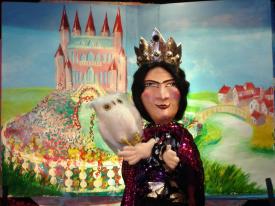 Reine de la Colline au rose devant un château rose et un jardin fleuri; sur la droit, une rivière, un pont et un village