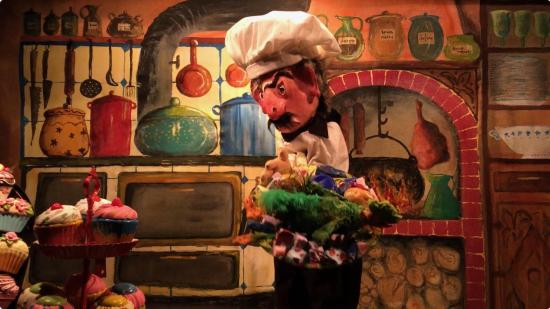 Maître Grognefour, une volaille dans les mains, devant un plateau de gâteaux