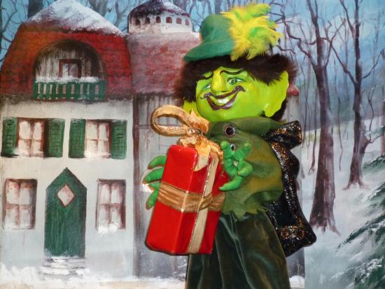 Garougriffou devant la maison de la femme au chignon rouge avec un paquet cadeau dans les mains