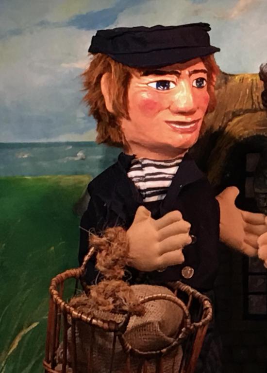 Homme brun, vêtu d'un habit de pêcheur, coiffé d'une casquette et tenant au bras un panier