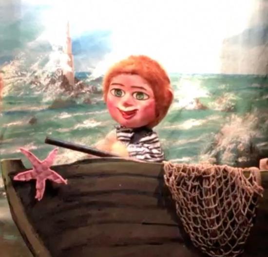 Garçon roux aux yeux bleus, vêtu d'un pull à rayures, sur la plage devant une barque