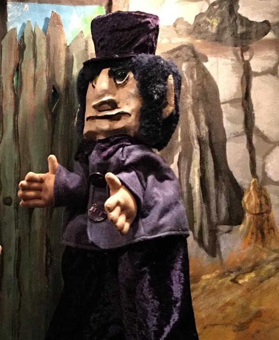 Homme noiraud, vêtu d'un pantalon et d'une veste violet foncé, coiffé d'un haut-de-forme noir