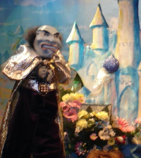 Vieil homme au visage gris, avec une calvitie, vêtu d'une costume brun foncé et d'une longue cape dorée