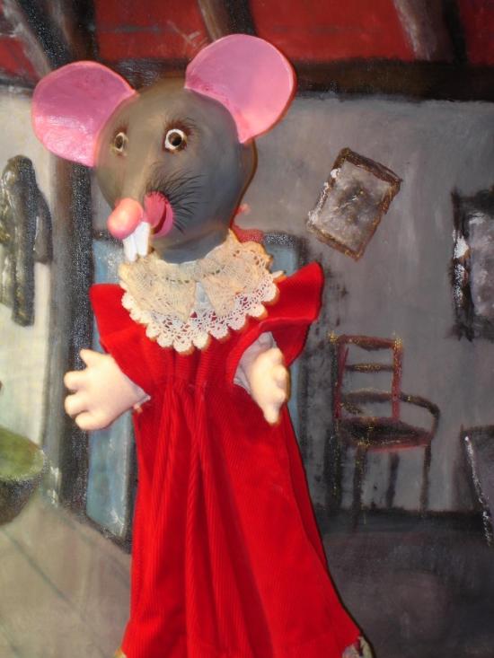 Souris grise au nez et aux oreilles roses, vêtue d'une robe rouge à col en dentelle, dans son grenier