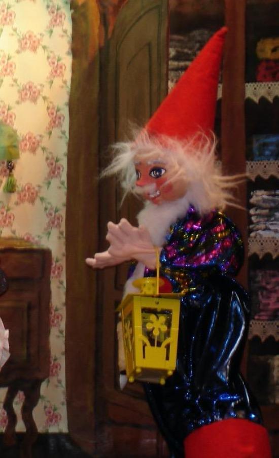 Lutin à barbe blanche devant une armoire ouvert, il tient une lampe dans sa main