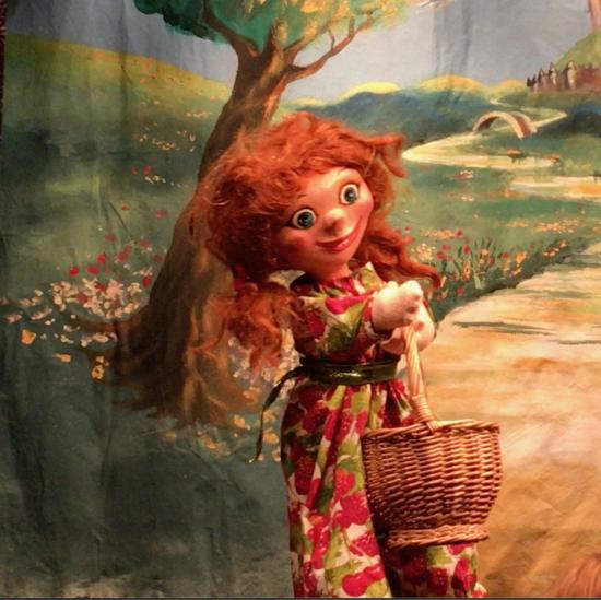 Jeune fille rousse vêtue d'une robe à motifs de fruits rouges, elle porte un panier et se trouve au bord d'une rivière