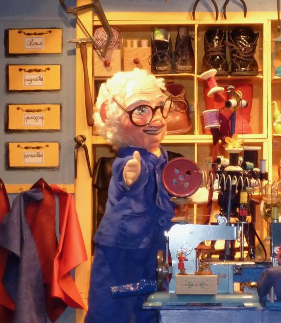 Léon le cordonnier à côté de sa machine à coudre et devant un étal de chaussures