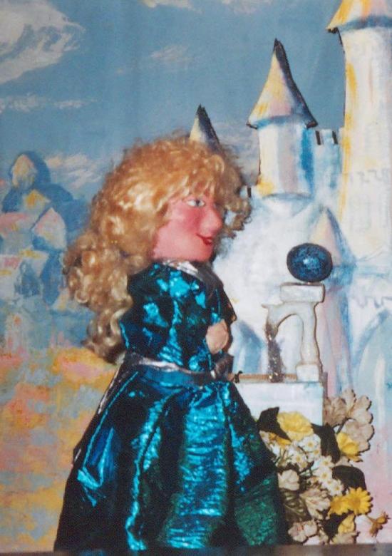 Jeune fille blonde aux yeux bleus, vêtue d'une robe bleue et d'un châle transparent, devant un château blanc