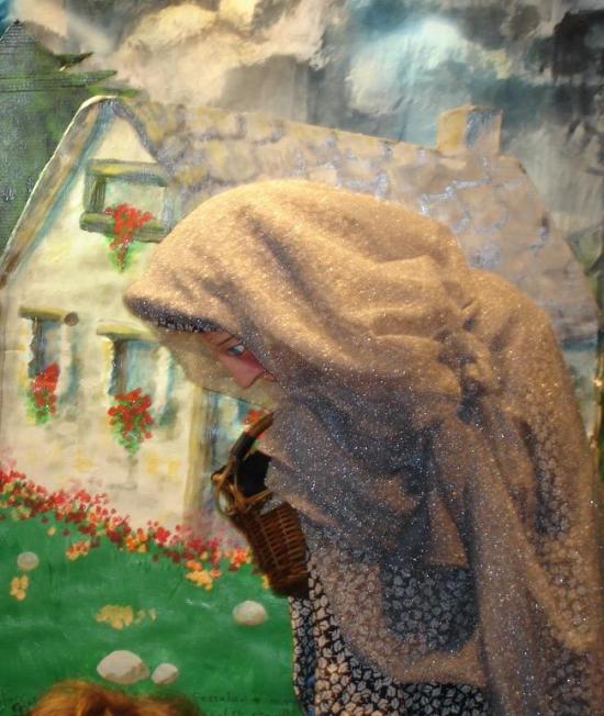 Vieille femme vêtue d'une robe bleue foncée à motifs, coiffée d'un voile qui lui cache le visage