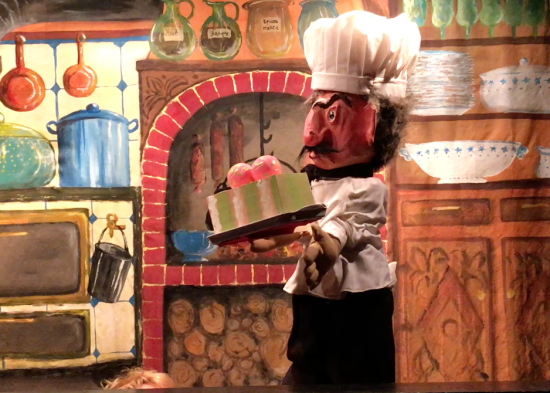 Maître Grognefour dans sa cuisine portant un gâteau