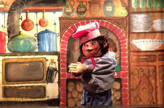 Léon Marmiton bossu dans sa cuisine, devant une cheminée et une cuisinière à bois couverte de marmites