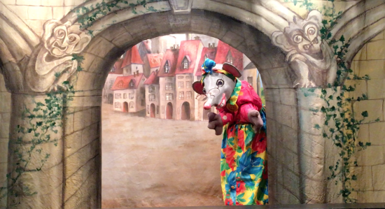 Fifi la Souris devant la porte voûtée d'un bourg