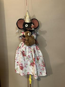 Fée souris vêtue d'une robe à fleurs blanche et rose et d'un tutu doré; elle porte un ours en peluche dans ses bras