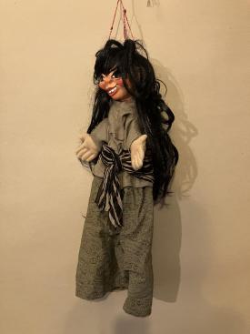 Jeune fille aux longs cheveux bruns décoiffés, vêtue d'une robe brun clair avec une ceinture à rayures