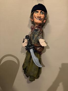 Homme brun aux yeux vairons, vêtu d'un pantalon vert et d'une casaque à rayures, coiffé d'un chapeau noir; il porte un sabre à la ceinture