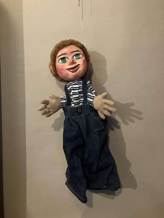 Garçon brun aux yeux bleus, vêtu d'une salopette grise et d'un pull à rayures