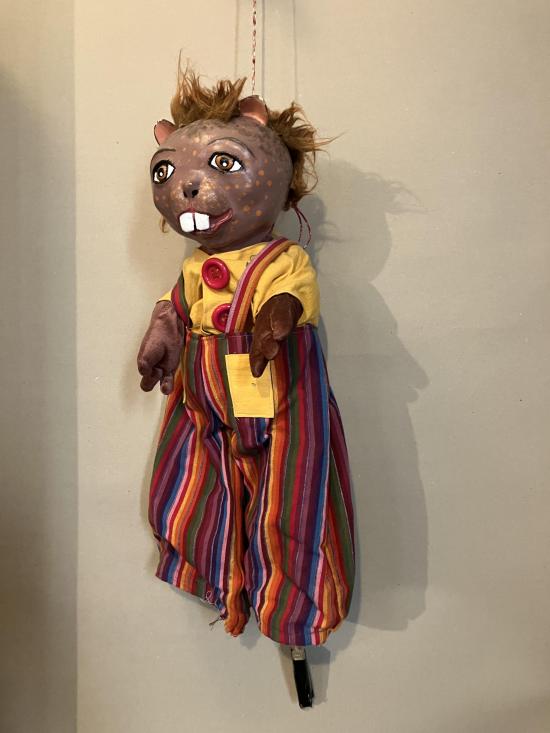 Castor vêtu d'une salopette à rayures multicolore et d'une chemise jaune