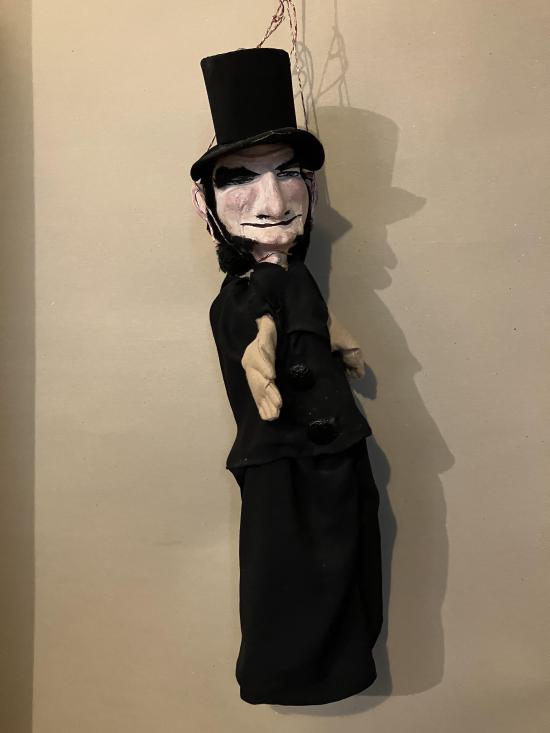 Vieil homme noiraud avec de gros favoris, vêtu d'un pantalon et d'une veste noires, coiffé d'un haut-de-forme noir