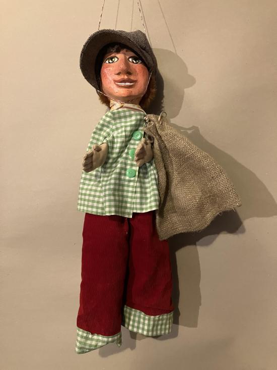 Jeune roux vêtu d'un pantalon rouge et d'une veste à petits carreaux verts et blancs, coiffé d'un chapeau brun