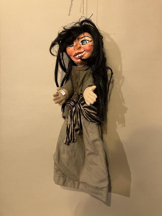 Jeune fille aux longs cheveux bruns décoiffés, vêtue d'une robe brun clair avec une ceinture à rayures