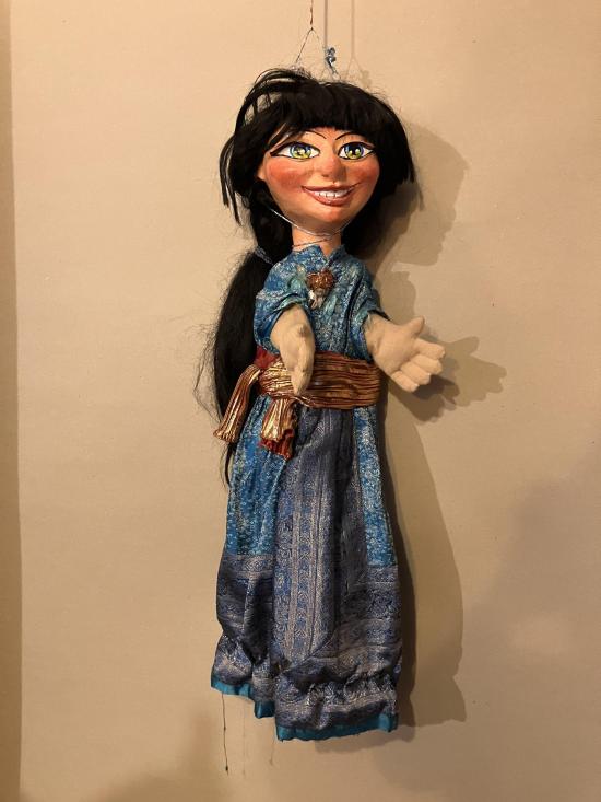 Jeune fille aux longs cheveux bruns, vêtue d'une robe bleue avec une ceinture brune et dorée