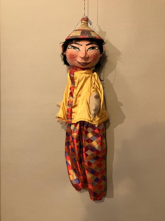 Jeune homme aux yeux bridés, vêtu d'un pantalon à losanges rouges et d'une veste jaune, coiffé d'un chapeau en paille