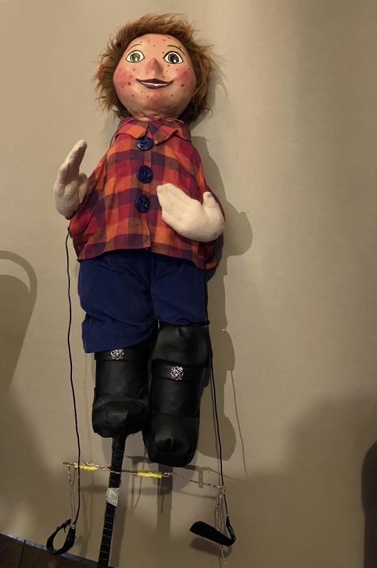 Jeune homme roux chaussé de grosses bottes noires, vêtu d'un pantalon bleu foncé et d'une veste à carreaux rouges