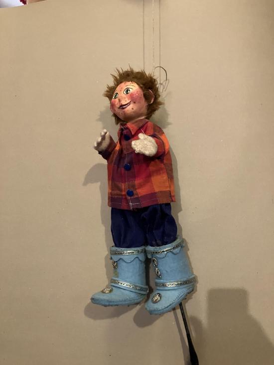 Garçon roux chaussé de bottes bleues claires, vêtu d'un pantalon bleu foncé et d'une veste à carreaux rouges