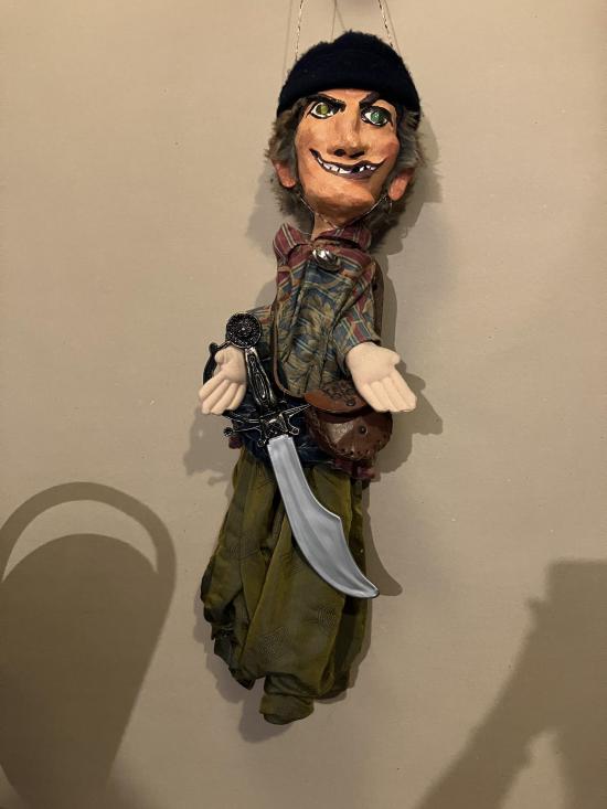 Homme brun aux yeux vairons, vêtu d'un pantalon vert et d'une casaque à rayures, coiffé d'un chapeau noir; il porte un sabre à la ceinture