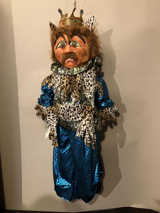 Tigre coiffé d'une couronne d'or, vêtu d'une tunique bleue et d'une cape en peau de tigre; il est triste