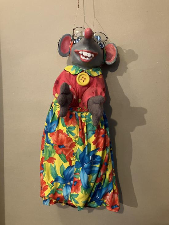 Souris grise souriante à lunettes et à grandes oreilles, vêtue d'une robe à fleurs et d'une blouse rouge