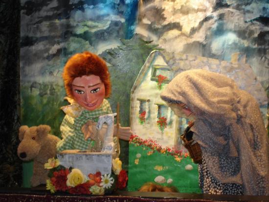 Jeannot et une vieille femme recouverte par un voile blanc, à côté de la fontaine et devant une maison