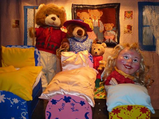 Boucle d'Or dans le petit lit, la famille d'ours debout derrière elle