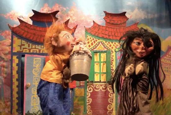 Youki avec un seau d'ordures dans les mains et Perle d'Or devant des maisons colorées