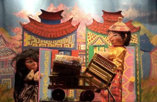 Perle d'Or et le marchand ambulant chinois, qui tient son charrette chargée d'un coffret et d'un métier à tisser, devant des maisons colorées