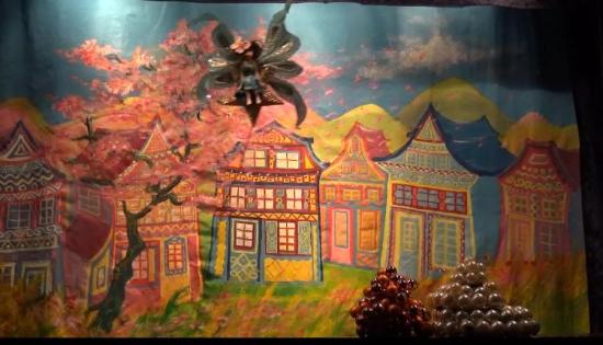 Fleuréroile en fée volette au-dessus de la place du village, maisons colorées et cerisier en fleurs roses