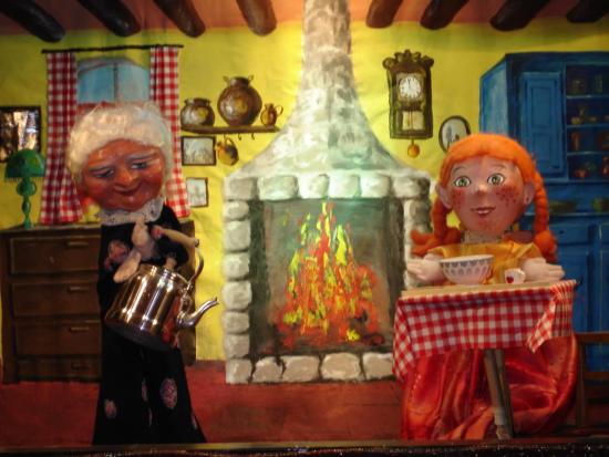 Mélodie assise dans la cuisine de Grand-Mère Louise qui tient une théière à la main; le feu brûle dans l'âtre