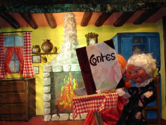 Mélodie assise dans la cuisine de Grand-Mère Louise ; le grand livre de contes est posé sur la table et le feu brûle dans l'âtre