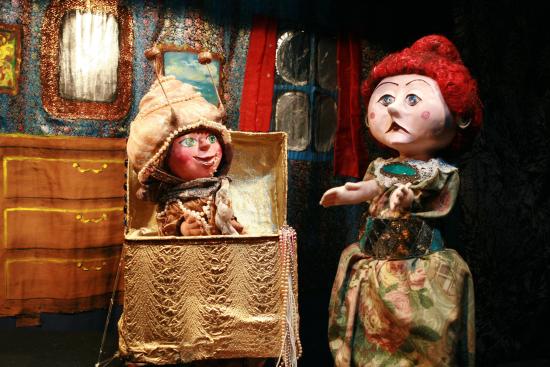 Dans un salon, Margote sort de son coffre, la femme au chignon rouge la regarde