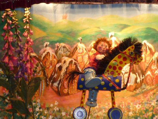 Théo bébé sur son cheval de bois, devant un village dont les maisons sont en chocolat, crème et gâteau