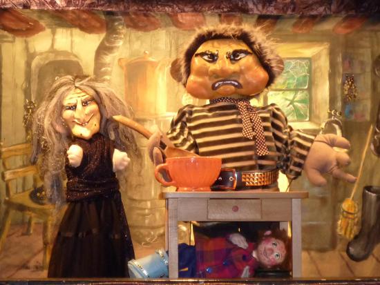 Croc'Peton et sa mère debout dans la cuisine, Théo caché sous la table