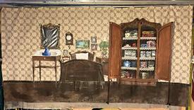 Chambre à coucher avec un lit, une table sur laquelle est posé un broc et une armoire à portes ouvertes