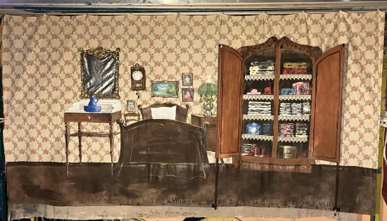 Chambre à coucher avec un lit, une table sur laquelle est posé un broc et une armoire à portes ouvertes