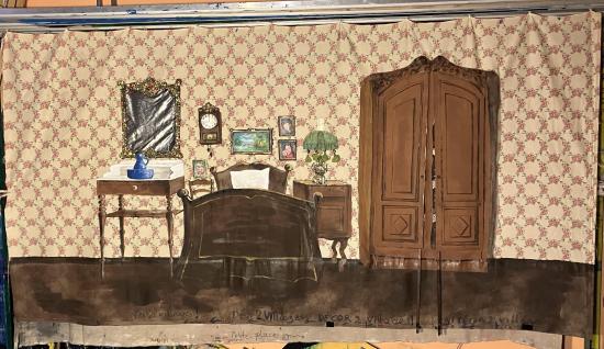 Chambre à coucher avec un lit, une table sur laquelle est posé un broc et une armoire à portes fermées